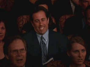 Animated GIF of a man in a theater audience grinning with excitement.